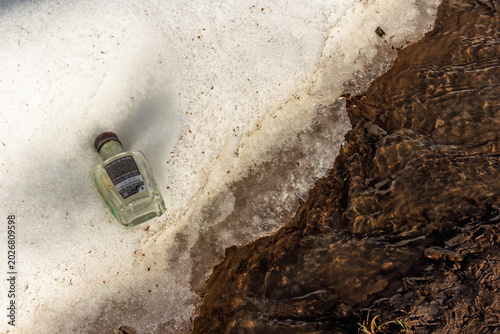Canvas Print Discarded glass bottle lying on thawing road shoulder snowbank near melting spri