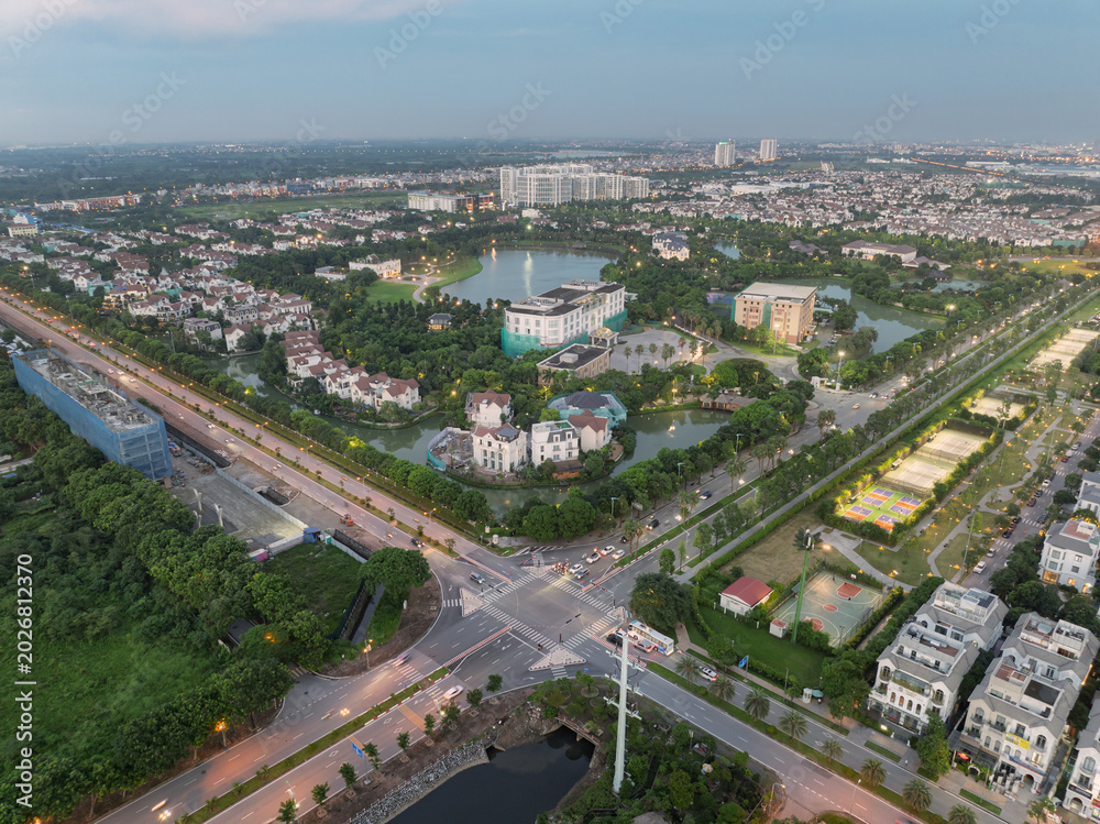Fototapeta premium Evening aerial photograph of a green urban enclave with villas, roads, and illuminated intersections in Long Bien, Hanoi.