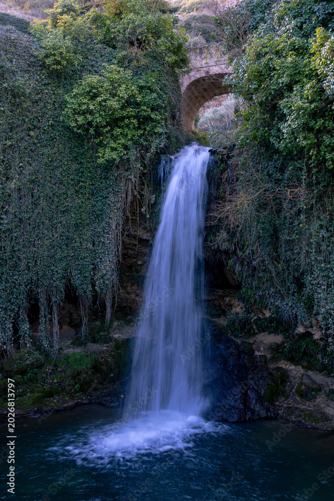 Obraz premium Scenic waterfall with metal water gate flowing between traditional stone houses in a rural village
