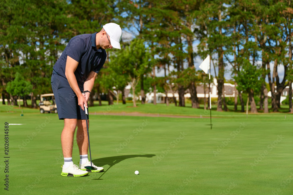 Obraz premium Man putting golf ball on green course.
