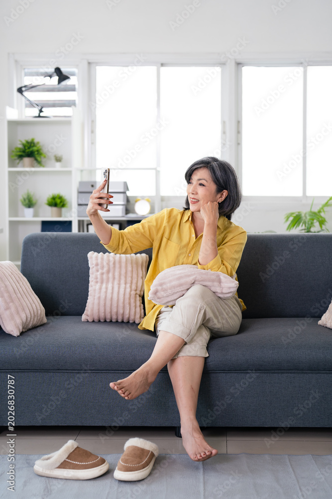 Obraz premium Cheerful elder mature woman talking on video conference call at home, holding smartphone,smiling enjoying online conversation.