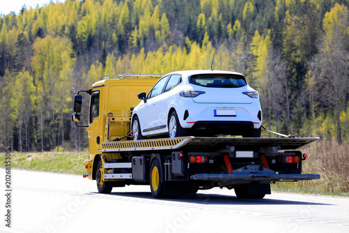 Yellow Flatbed Tow Truck Carrying White Car along Highway.