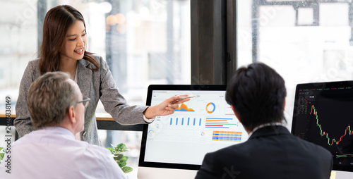 Asian businesswoman pointing at dashboard chart during meeting with business partners