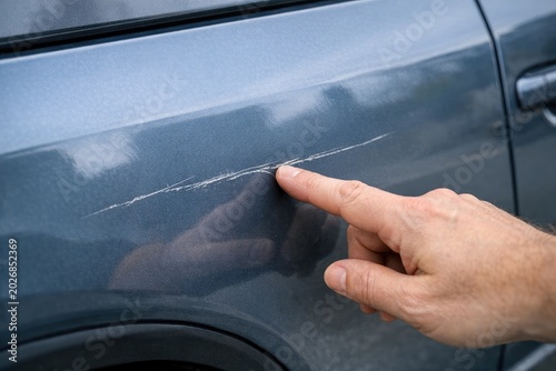 A person's hand points out a crack on the side of a car, indicating damage or potential issues