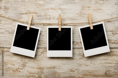 Three blank instant photo frames hanging on clothesline with wooden pegs over rustic wood background