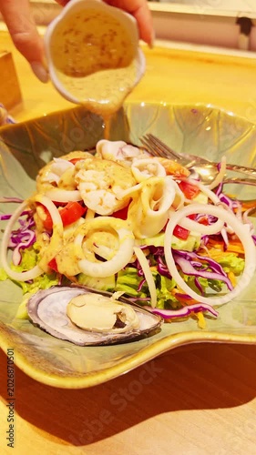 Vertical video. Fresh Seafood Salad With Squid Rings Shrimp Mussel and Vegetables While Creamy Dressing Is Poured Above Bowl, Gourmet Healthy Eating