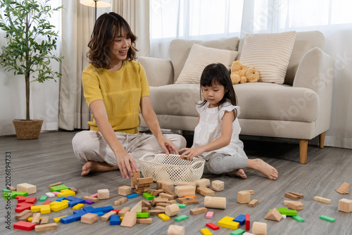 Tableau sur toile Asian mother teaching daughter good habit through cleaning toys, child placing b