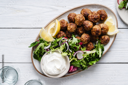 Meatballs served green salad and yogurt based dip on tray, comfort food