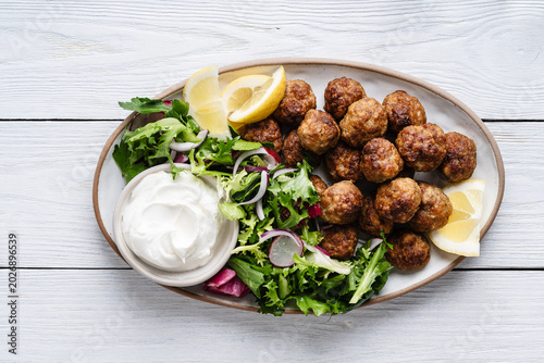 Meatballs served green salad and yogurt based dip on tray, comfort food
