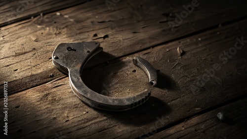 restraint. A broken metal handcuff on old wooden floorboards, dramatic side lighting creating shadows. public awareness campaigns.