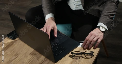 Internet scammer shows bank card while working on laptop at coffee table. Man in suit types messages as presents payment card to support deceptive online scheme