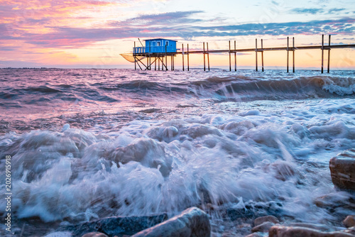Photos Cabane de pêcheur sur pilotis au coucher du soleil, vagues et écume sur les gale
