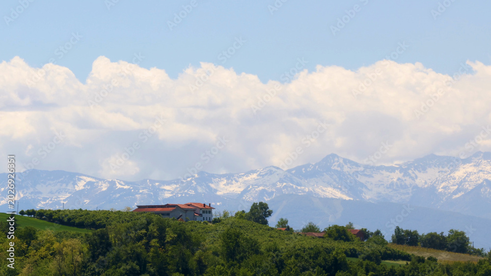 Fototapeta premium Snowy Alps Mountains Behind Green Rolling Hills and Italian Farmhouse