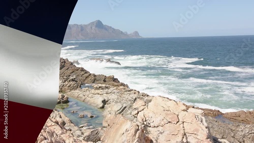 Rocky shore and ocean sending breaking waves while wind causing flag flapping, showing surf motion