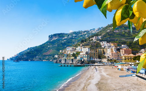 Scenic view of Minori town with sandy beach and blue sea water on Amalfi coast in Italy. Yellow lemons on branches frame beautiful Mediterranean landscape under sunny sky 