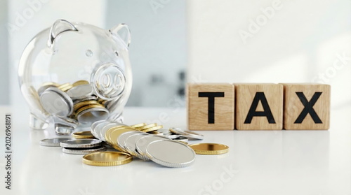 Tax savings with transparent piggy bank and money coins beside wooden blocks on white table, symbolizing fiscal responsibility.