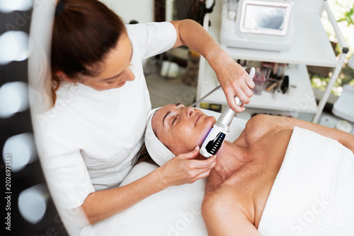 A professional aesthetician uses advanced beauty roller technology for skin tightening and body contouring on a relaxed client in a spa salon.
