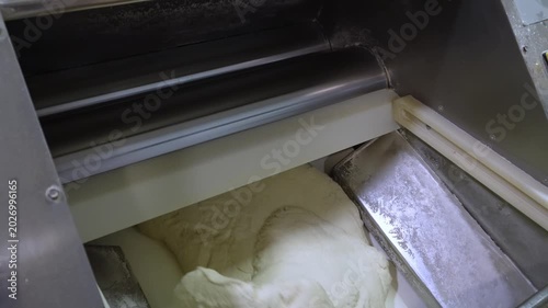 Close-up of an automated dough sheeter in a bakery processing raw dough. The professional equipment is laminating and kneading the mass for making bread