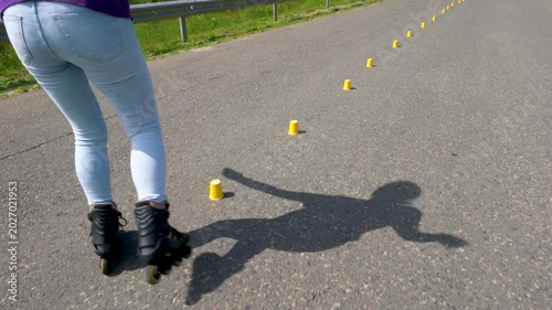A woman in jeans learns to skate on roller skates. She does special exercises while driving through the chips.