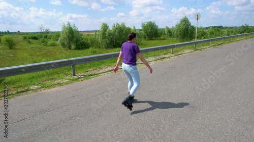 An adult woman in jeans is riding on roller skates along an asphalt road.