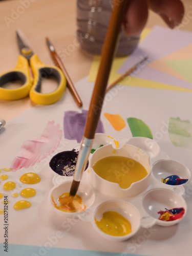 Фотография Close-up of a Child Dipping a Paintbrush into Yellow Paint Palette