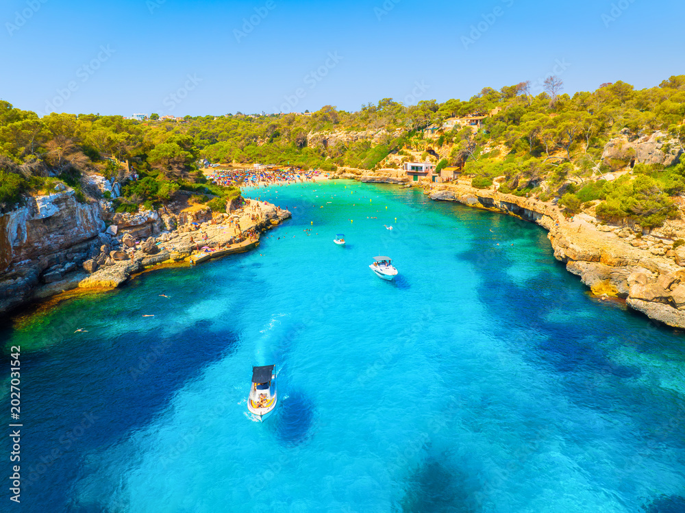 Obraz premium Aerial view of a boat in a Llombards beach, Mallorca, Spain. Summer vacation concept with azure Mediterranean water, scenic coastline and drone landscape. Travel and relaxation in the sun.
