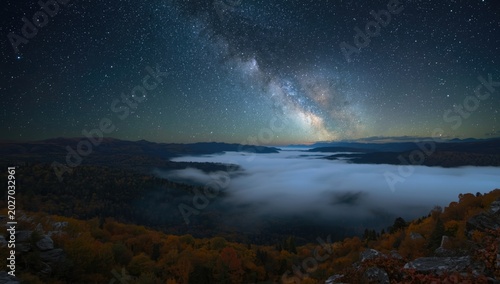 Aerial autumn night view of mountain valley blanketed in fog under Milky Way sky