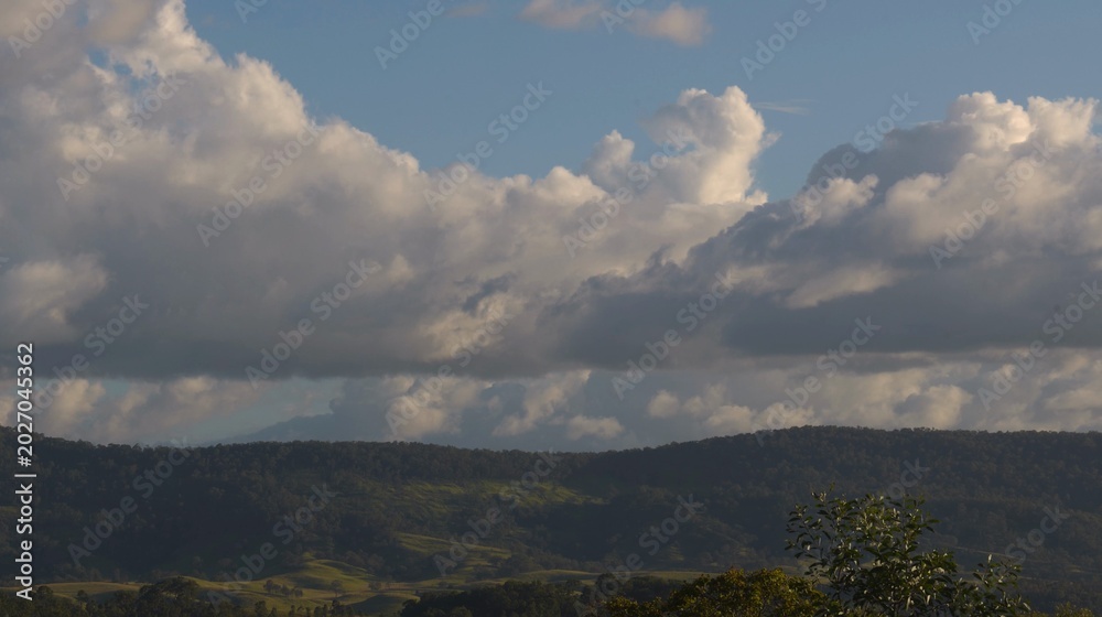 Fototapeta premium Large White Cumulus Clouds Floating Over Lush Green Rolling Hills