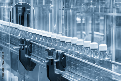 Quadro su tela Automated mass production line of drinking water with a row of clear plastic PET bottles on a conveyor belt