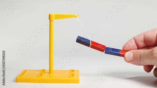 Schilderij op canvas Hand Demonstrating Magnetic Attraction with Suspended Red and Blue Bar Magnets