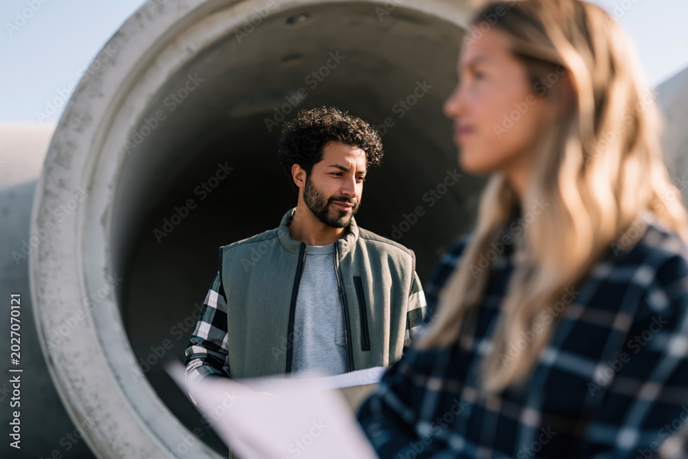 Fototapeta premium Construction workers inspecting large concrete pipe at a site with male and female engineers for industrial background and teamwork banner design