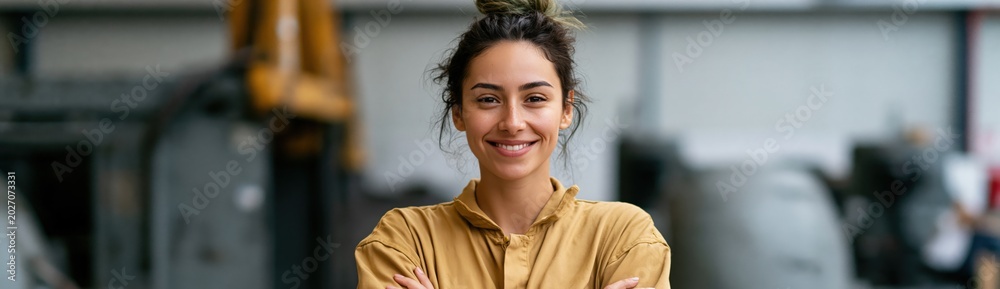 Fototapeta premium Confident female factory worker portrait in workshop background for industrial recruitment banner and workplace design