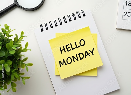 Yellow sticky note with hello monday text placed on a white spiral notebook on desk