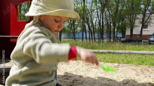 Child plays in sandbox with green shovel in sunny park