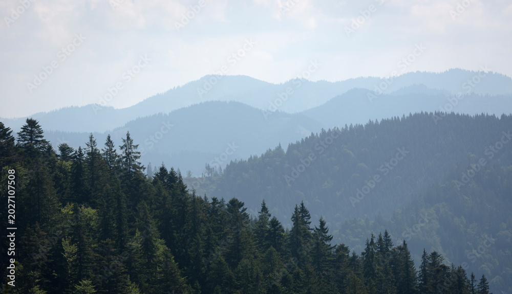 Naklejka premium Stunning view of layered mountains with lush green forests and soft clouds