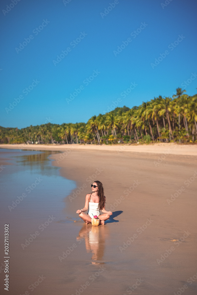 Obraz premium Woman meditating on tropical beach with coconut drink