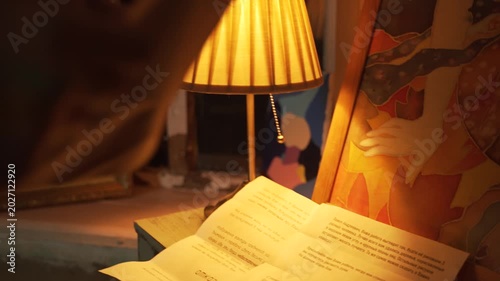 Man's hand turns on table lamp with a bright light. There is letter and picture on the table