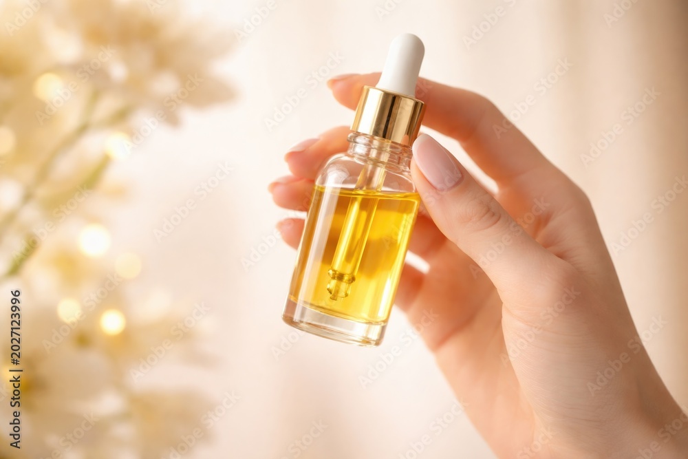 Fototapeta premium Yellow oil dropper contained in a clear jar held delicately by a feminine hand with beauty theme and copy space