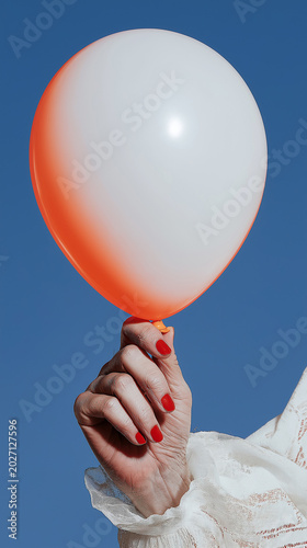 Close-up of a hand with red nail polish holding a white balloon with an orange rim on a clean blue background. Minimal party concept for social media, greeting cards and celebration branding.