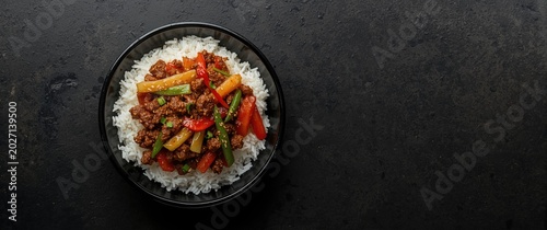Bowl of Ground Meat and Vegetable Stir-Fry on White Rice Dark Countertop, Top View, Copy Space