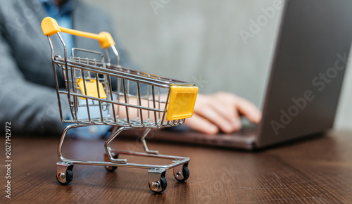 Foto Close-up of empty shopping cart with laptop in background, showing e-commerce, online marketplace, abandoned cart, digital shopping and retail strategy