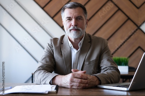 Smiling mature business man executive wearing shirt sitting at desk using laptop. Happy busy professional middle aged manager investor working on computer in office