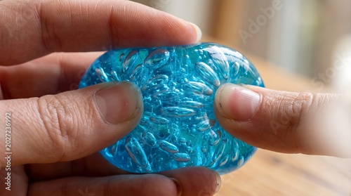 Squeezable Jelly Ball: Macro shot of a transparent, squishy blue jelly ball being squeezed, showing air bubbles stretching inside its soft, gelatinous matrix.