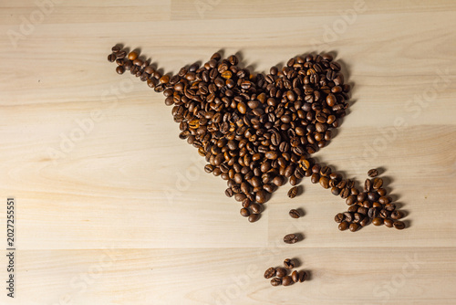 Roasted coffee beans arranged in a heart shape pierced by an arrow on light wooden background with copy space. Concept of love, romance and Valentine’s Day with coffee theme