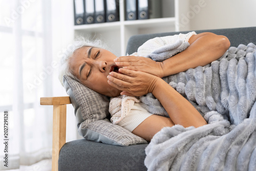 Fotografi Senior woman suffering from illness at home, resting on a sofa under a blanket