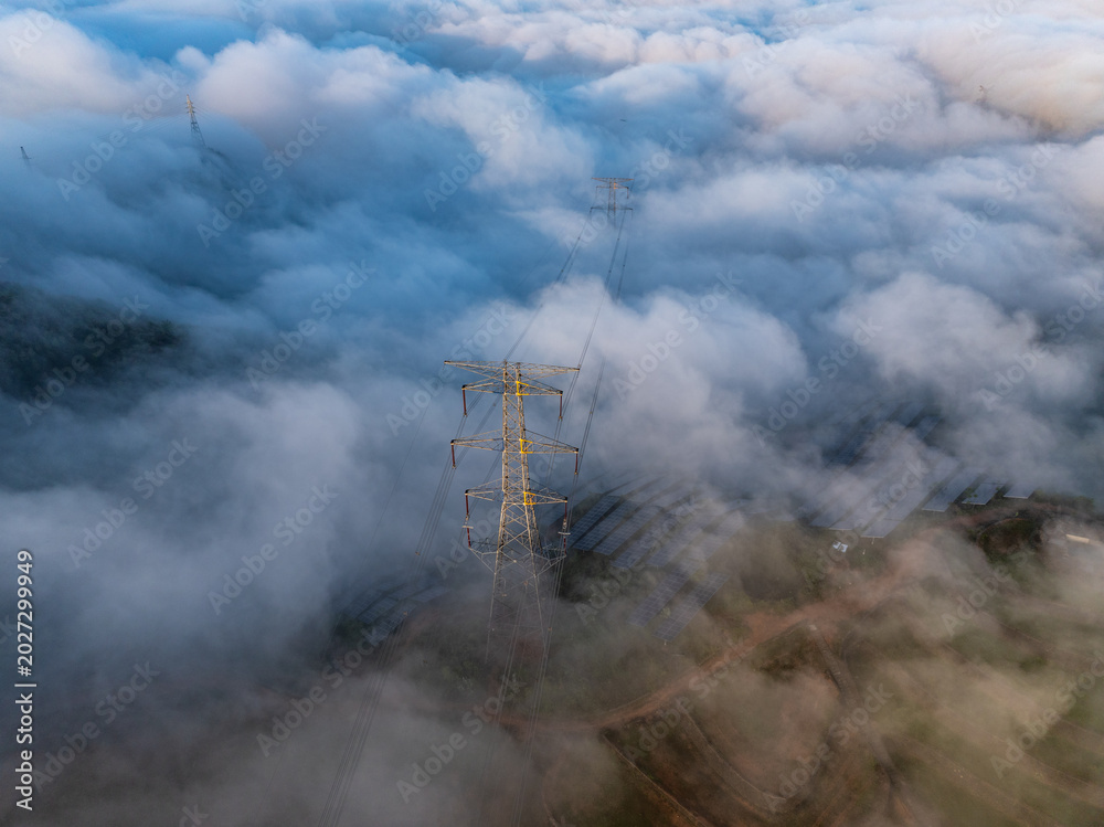 Fototapeta premium High voltage transmission tower standing amidst a sea of clouds in the mountains
