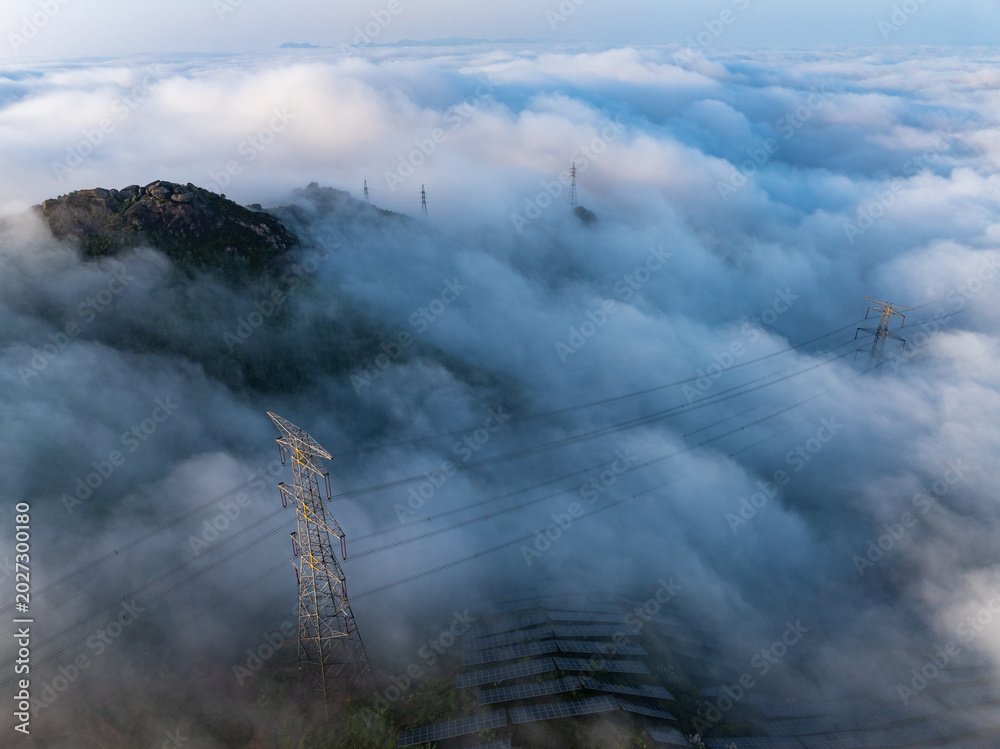 Fototapeta premium High voltage transmission towers standing above the sea of clouds and mountains
