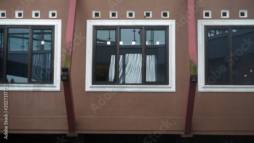 Foto Neat row of windows on brown building facade with white frames, decorative vents, and curtains visible inside