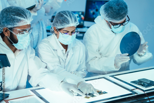 Obraz na plátně Group of semiconductor microchip engineers in protective cleanroom suits collabo