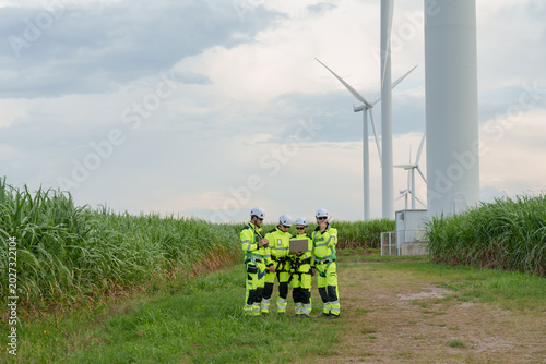Engineers gathered near turbine tower outdoor wind farm field reviewing operation using tablet maintenance task renewable power project supporting green energy technology teamwork sustainable